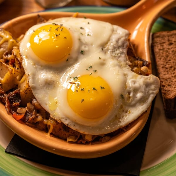 Breakfast hash topped with two fried eggs, served with dark bread on a striped plate.