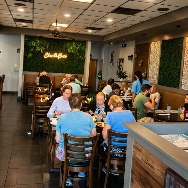 Busy restaurant interior with customers dining at tables, booths, and a bar, featuring a "Good Vibes" neon sign.