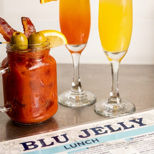 Bloody Mary with bacon and olives, two mimosas, and a Blu Jelly lunch menu on a counter.